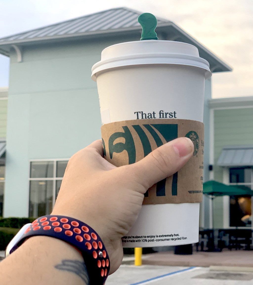 hand holding a cup of pumpkin chai in front of starbucks store