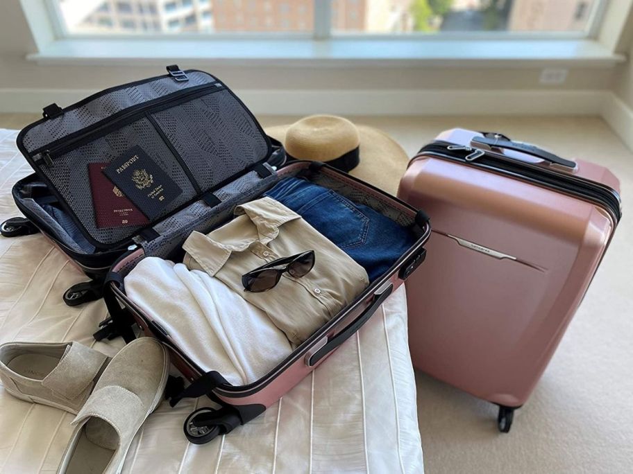 pink samsonite luggage on bed with clothes inside and suitcase sitting next to the bed