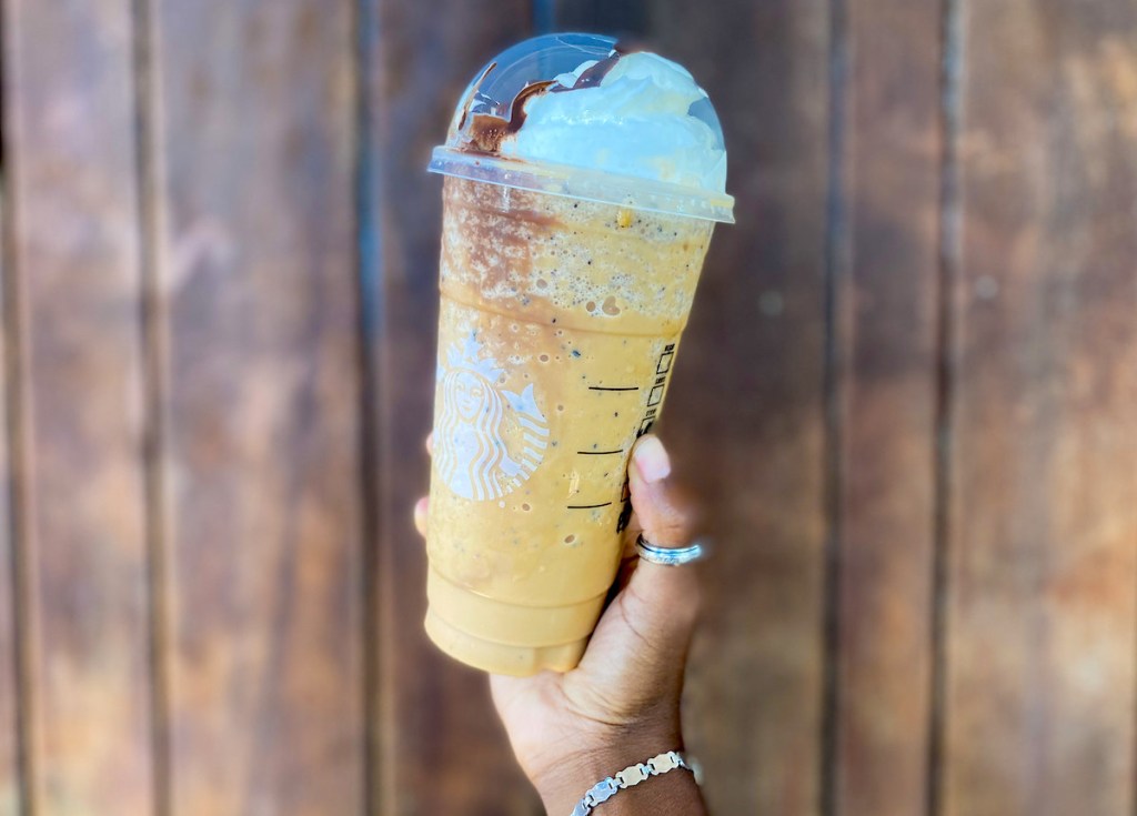 hand holding a starbucks frappuccino in front of wood wall