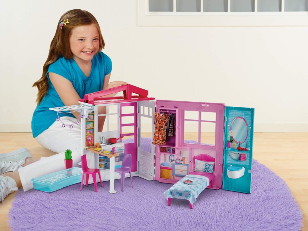 little girl sitting on the floor playing with a barbie dollhouse