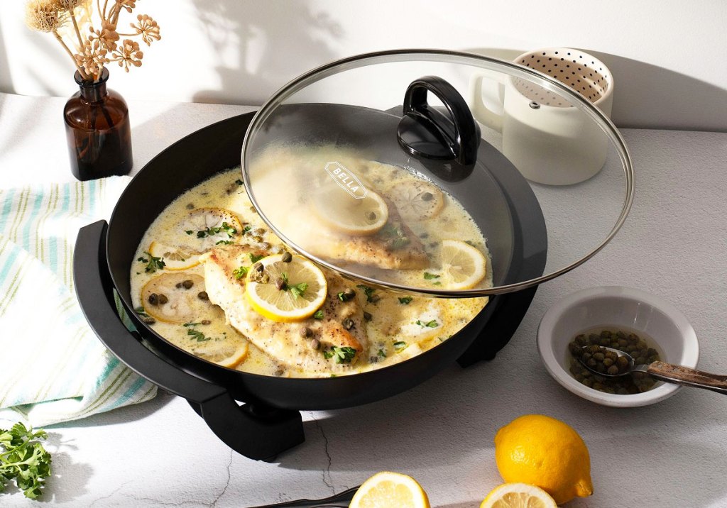 black round electric skillet on counter with lemon chicken dish cooking inside with a glass cooking lid