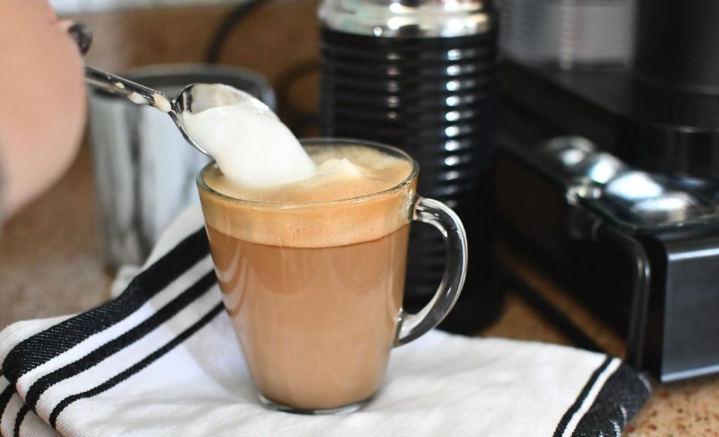 A hand pouring some milk froth into a cup of coffee