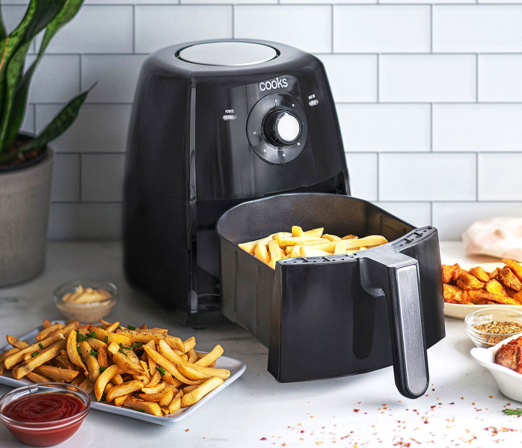 black air fryer on kitchne counter with fries in basket and fried food on plates around it