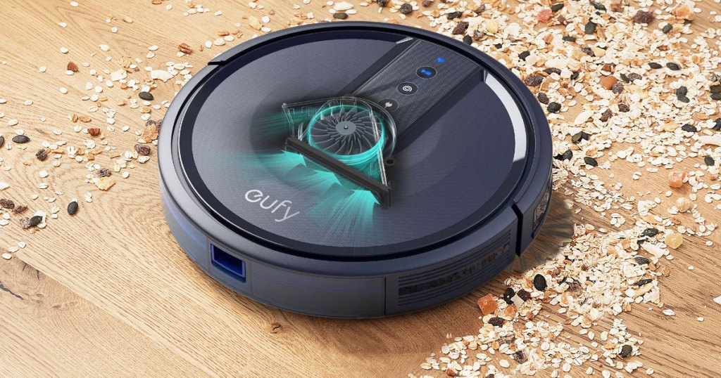 black eufy robotic vacuum cleaning up birdseed spilled on a wood floor