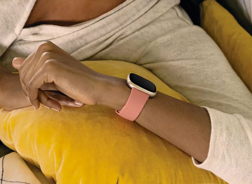 woman in a light grey sweater holding up her wrist to check a pink and gold fitbit