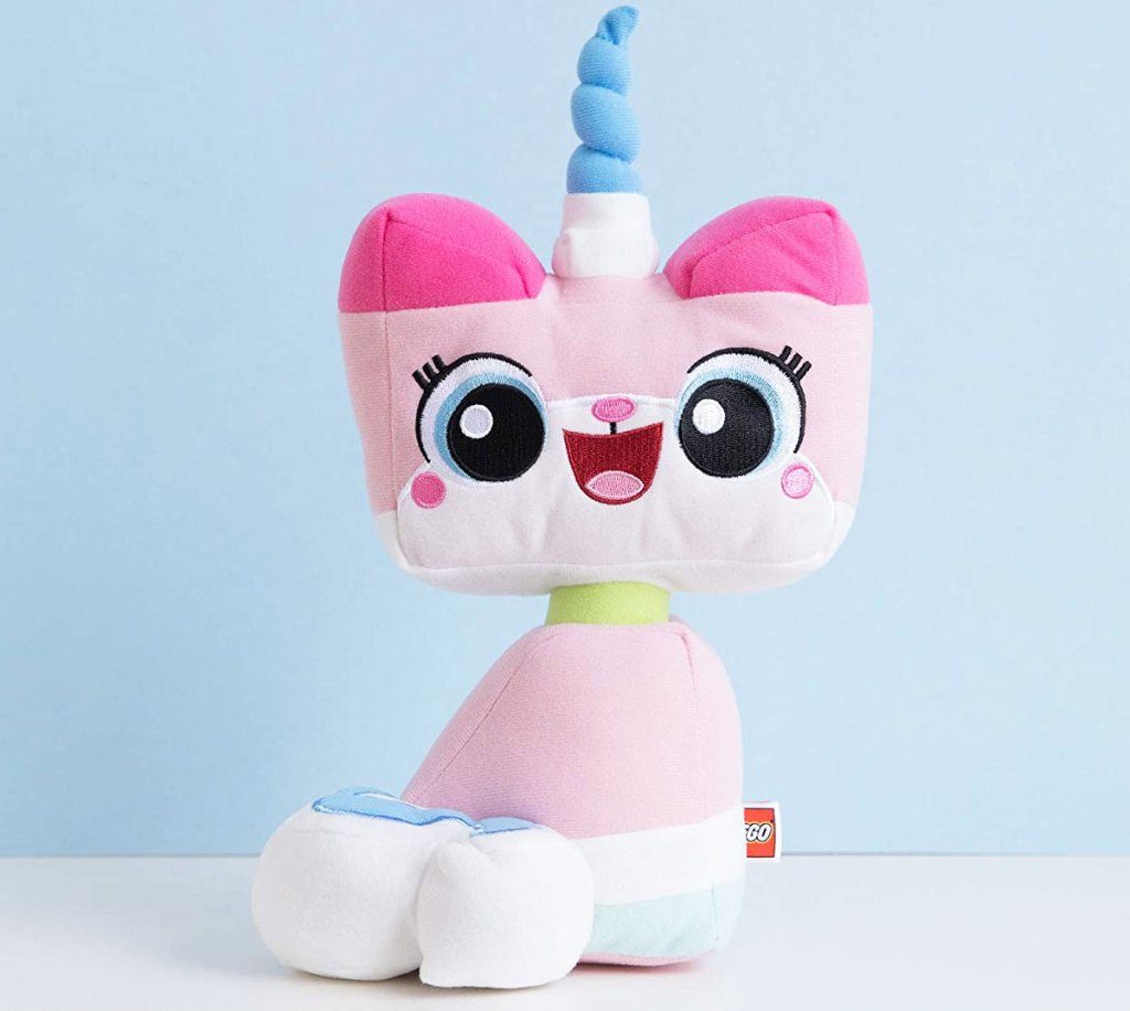 pink lego unikitty plush toy with blue unicorn horn sitting on a white table with blue background