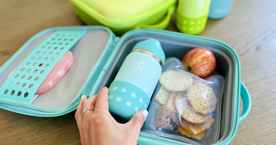 hand holding water bottle inside blue insulated hydro flask lunch box with food