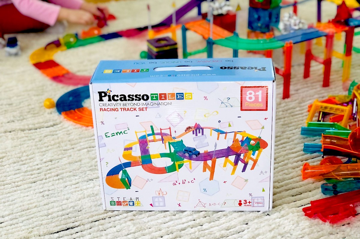 box of picasso tiles set sitting on carpet with race track behind it