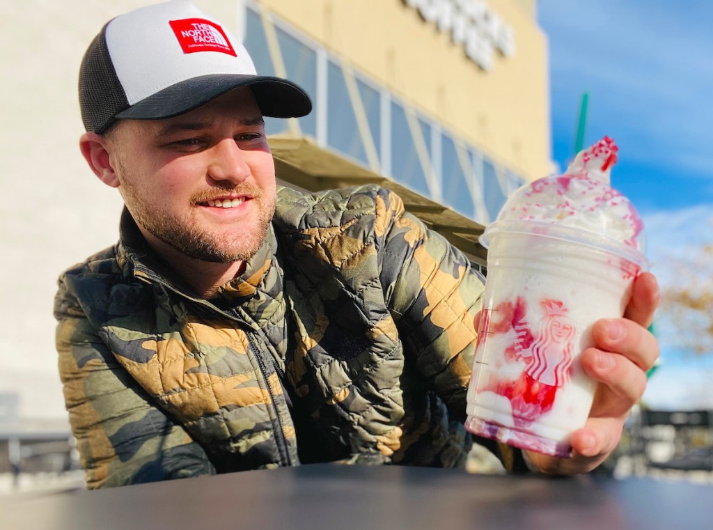 man holding a santa frappuccino sitting outside of starbucks