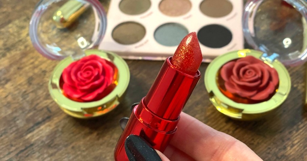 holding Winky Lux lip balm in a red sparkling color with makeup in background