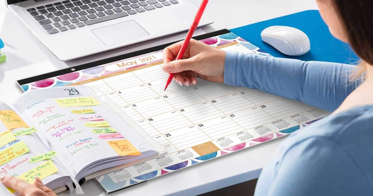 woman holding a red pen writing on a desk calendar