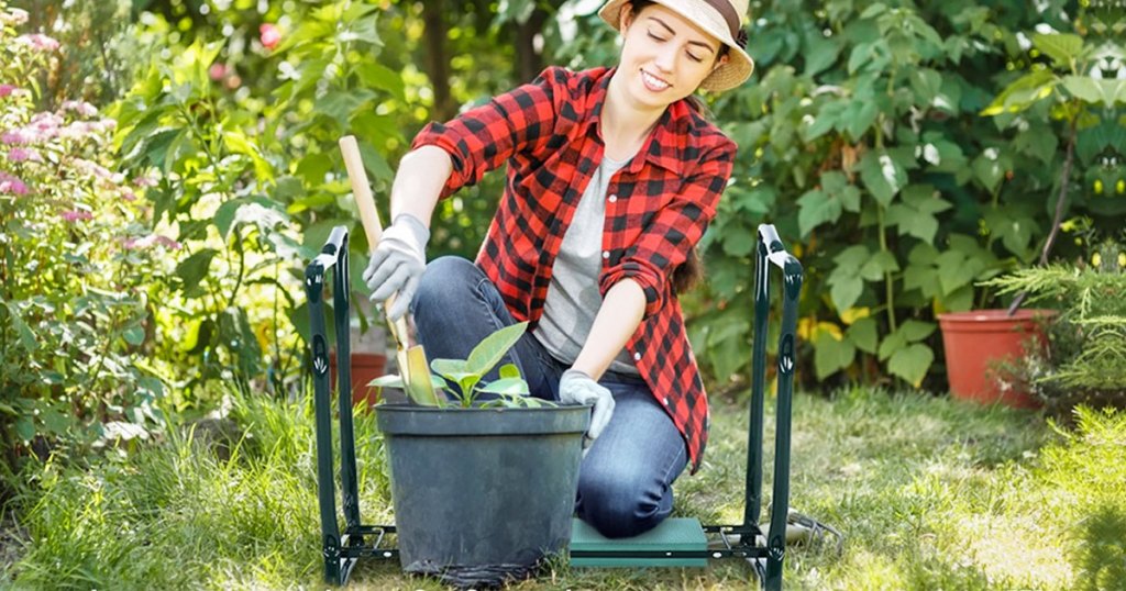 woman in jeans an red and black buffalo plaid shirt kneeling on garden bench to fill up a flower pot