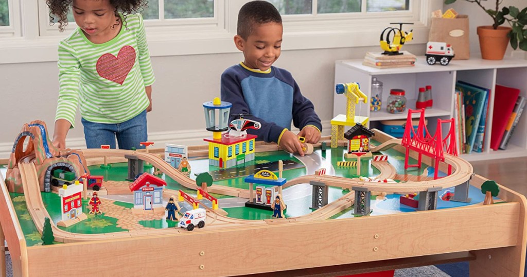 2 children playing with a large wooden train table set