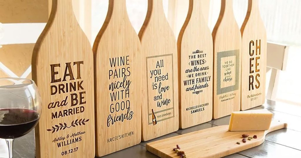 multiple wine bottle shaped wood cutting boards with wine-themed signs on them all lines up near a glass of wine