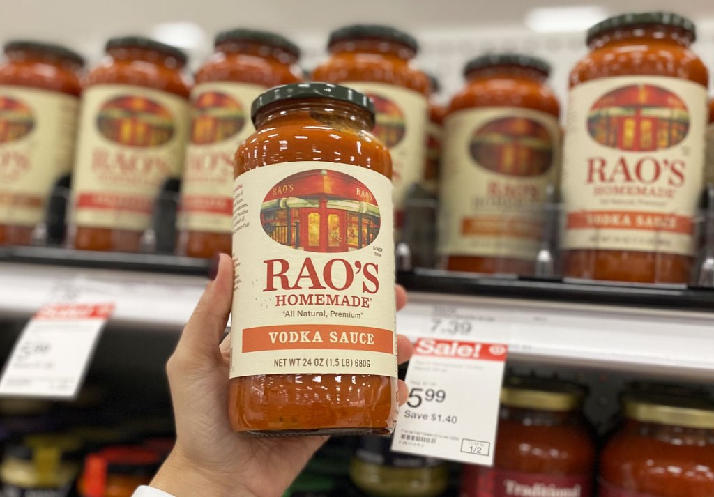 person holding up a jar of rao's vodka sauce in front of more rao's sauce on target shelf