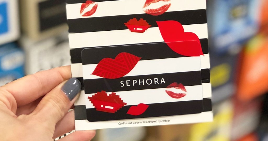 woman with grey nails holding up a white and black striped sephora gift card with red lips printed on it