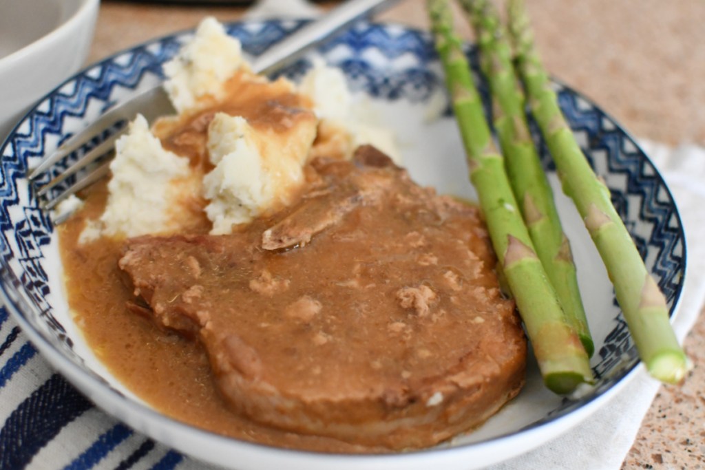 Easy slow cooker pork chops on a plate with mashed potatoes and asparagus