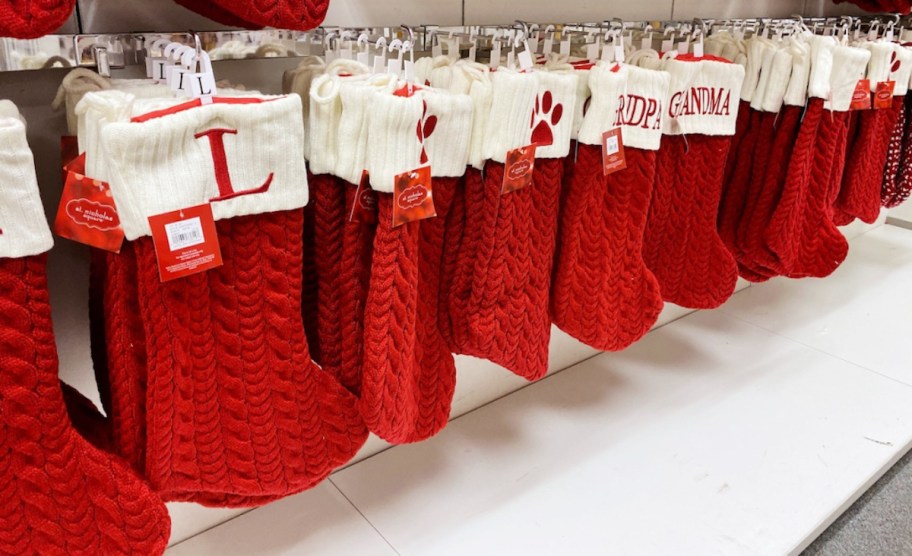 in store shelf with multiple monogram st nicholas square knit stockings in red