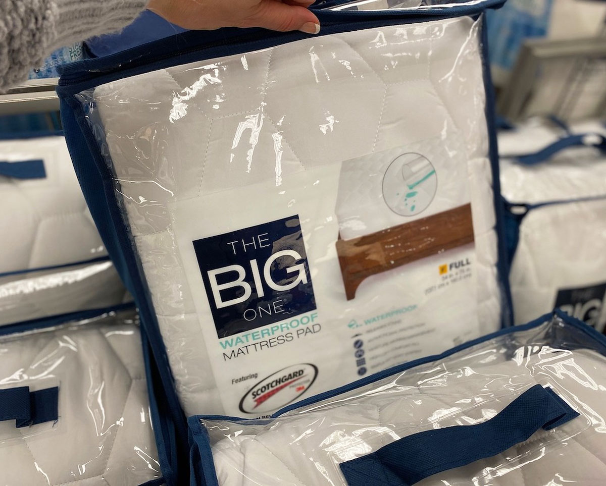 woman holding up a big one waterproof mattress pad from a display of multiple mattress pads