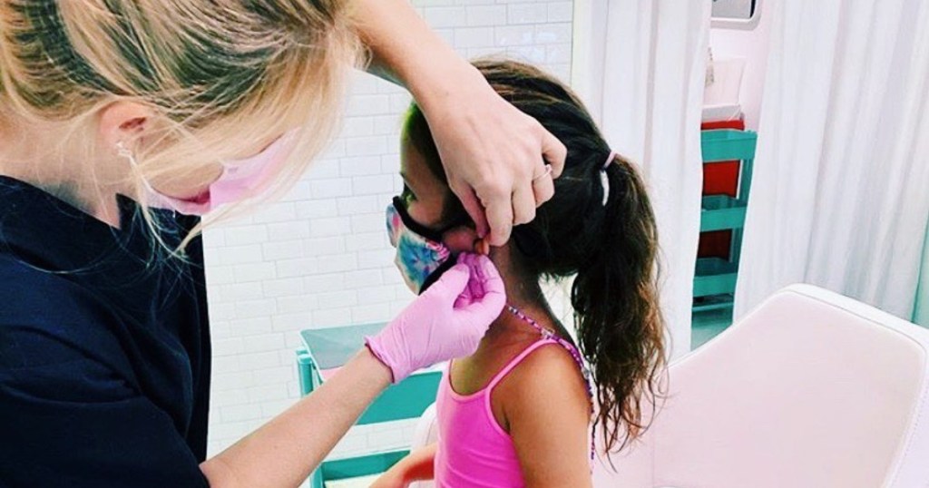 girl getting ears pierced by masked nurse