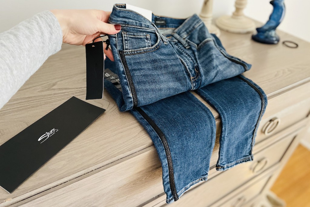 hand holding up a pair of jeans on top of dresser