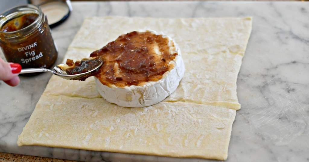 spreading fig spread on a wheel of brie