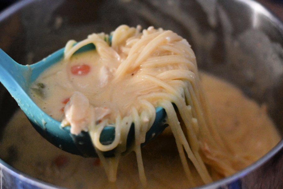 A cheesy chicken noodle soup with cream cheese on a ladle