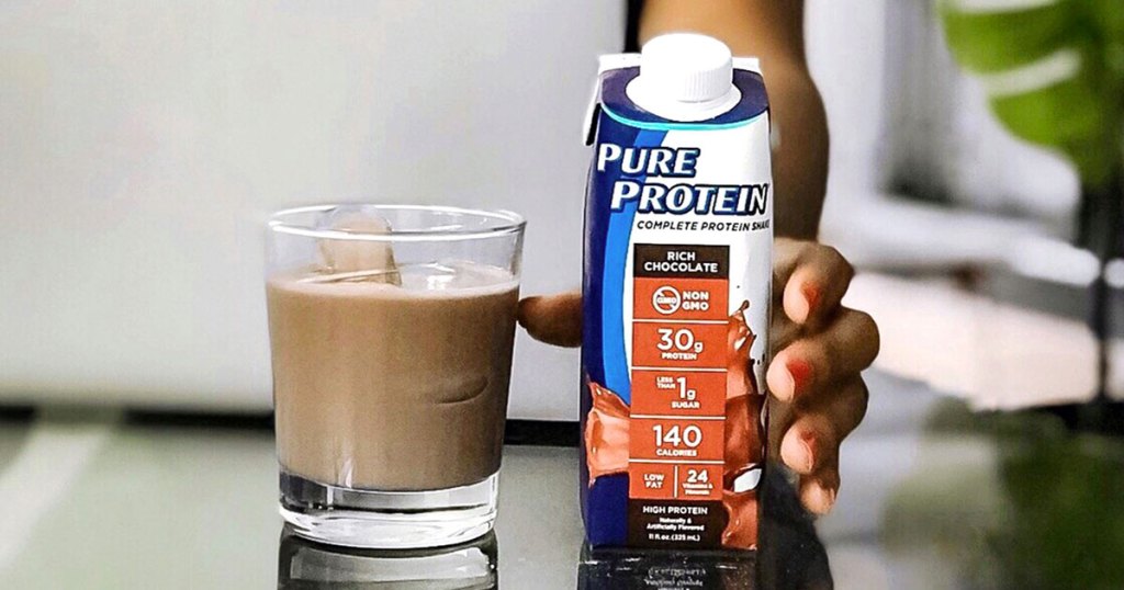 woman reaching for a pure protein shake next to chocolate protein shake in drinking glass