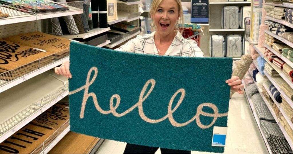 Woman holding up doormat that says hello