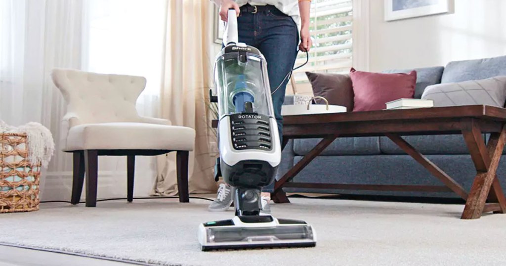 woman pushing a grey and white shark upright vacuum on area rug