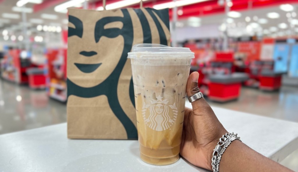 hand holding cookies and cream cold brew starbucks drink in front of bag