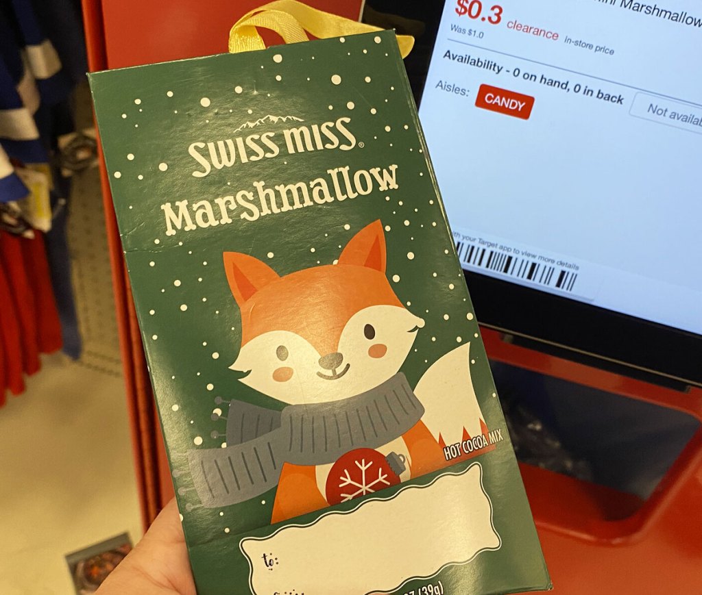 person holding up a green swiss miss hot cocoa packet ornament at a target price scanner