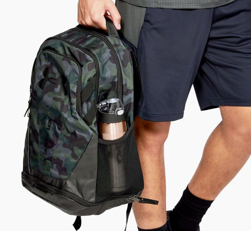 man holding a camo print under armour backpack