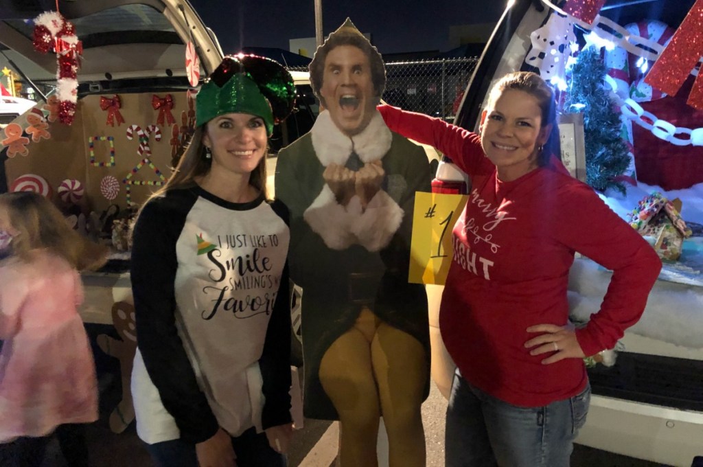 two women standing on either side of a buddy the elf cardboard cutout standee