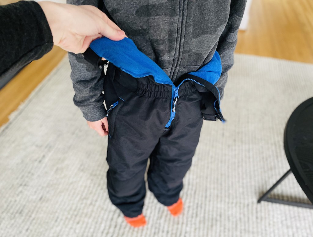 hand holding open a pair of black and blue kids snowpants