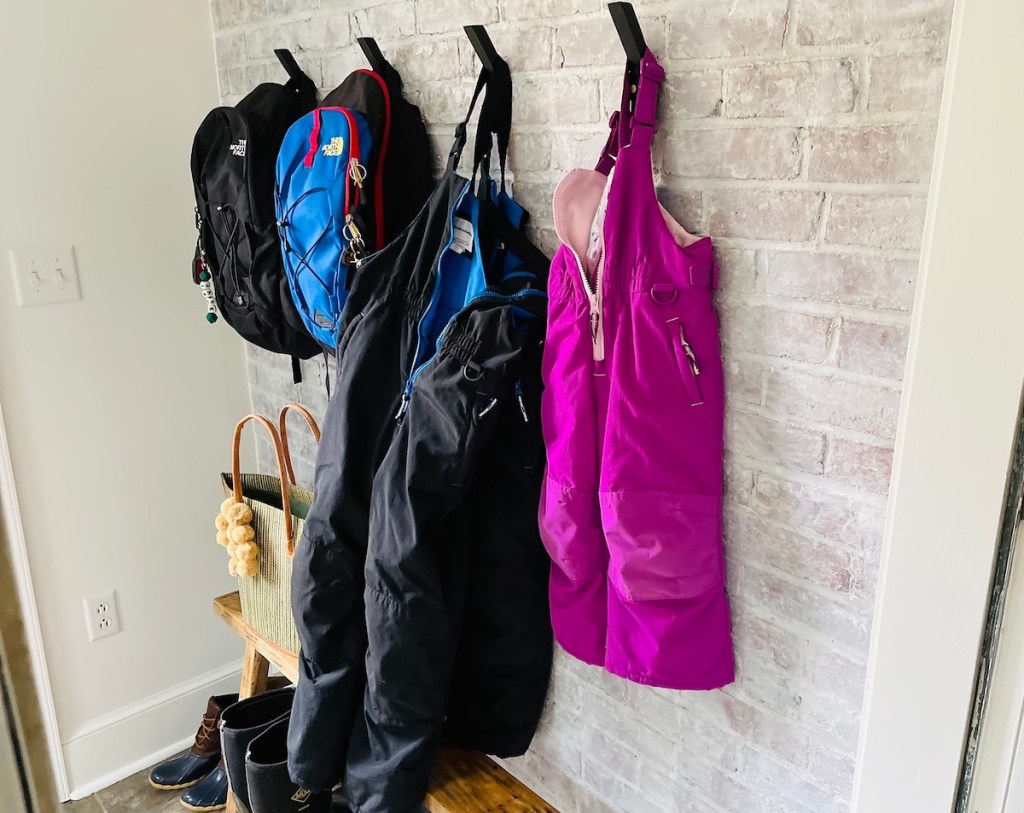 black and purple kids snow pants hanging in mudroom on brick wall