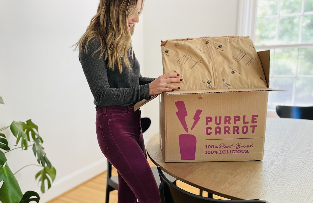 woman holding open purple carrot vegan meal kit on wood table