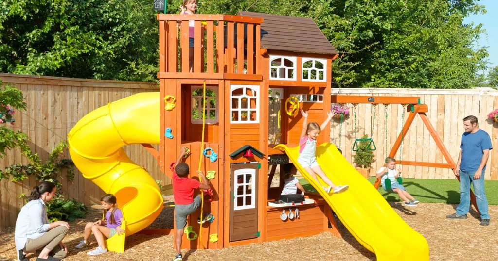 kids playing on wooden backyard playset with swings and multiple yellow slides