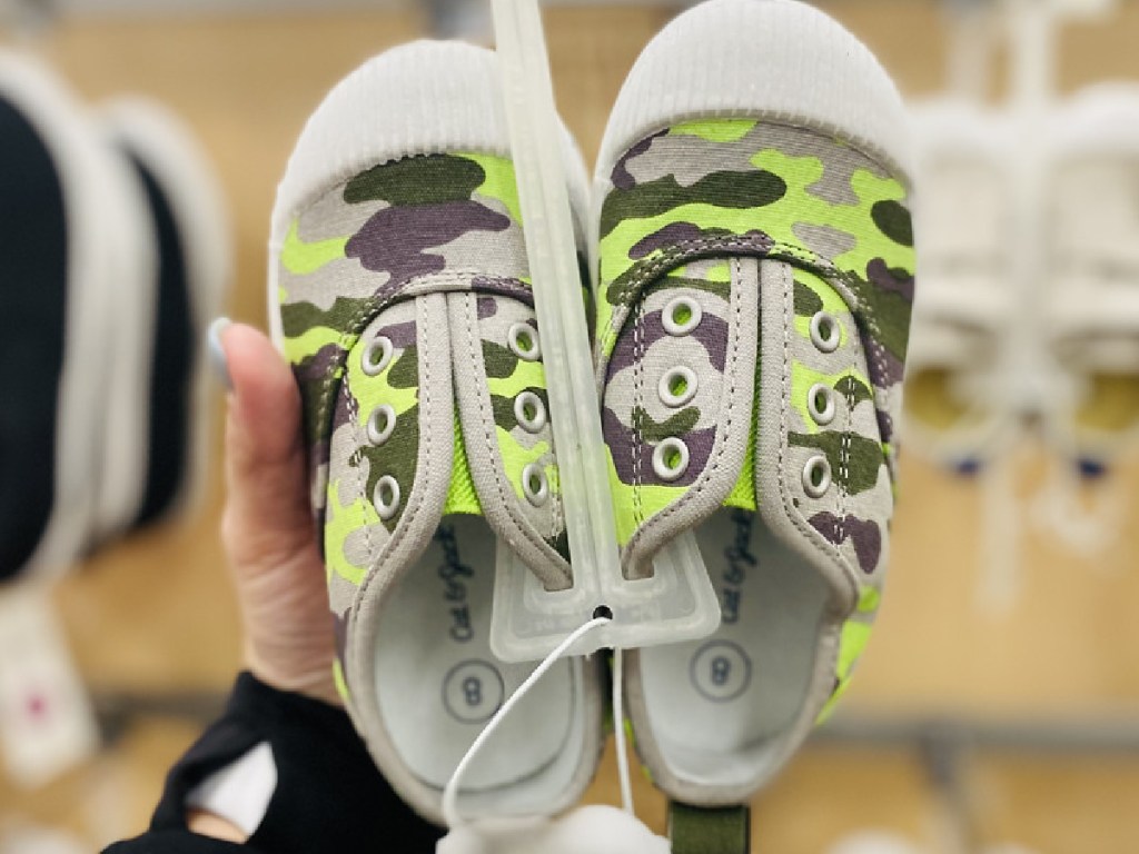 hand holding pair of kids shoes with camo design