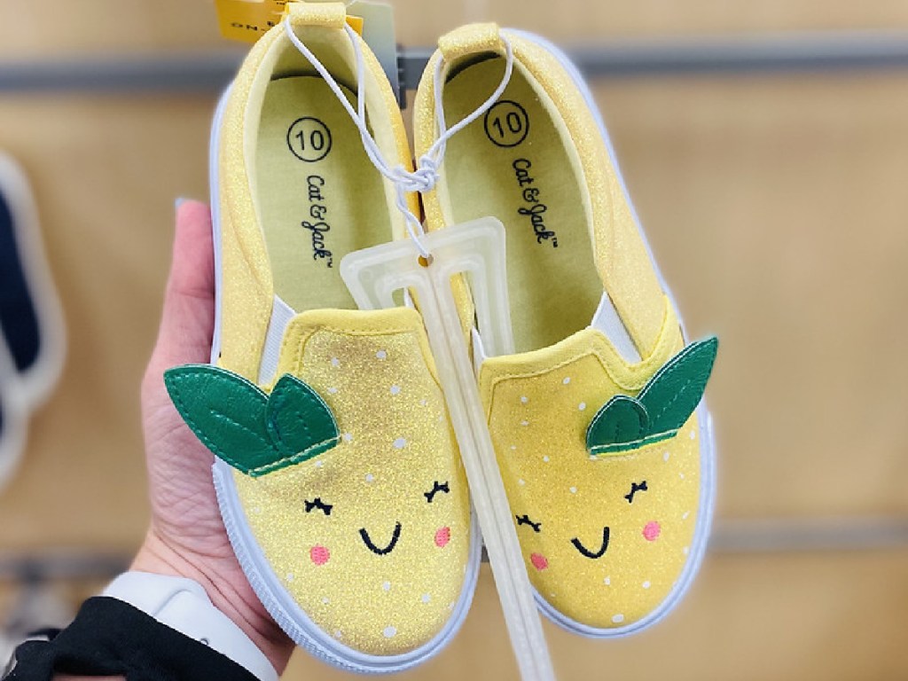 hand holding pair of yellow shoes for kids that look like lemons