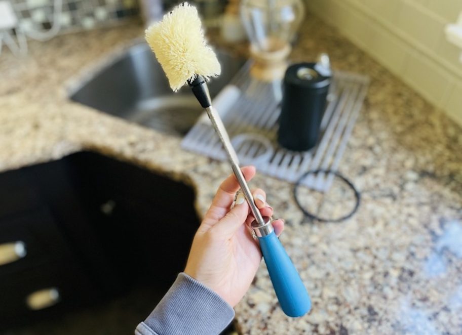 hand holding blue bottle brush in kitchen over sink