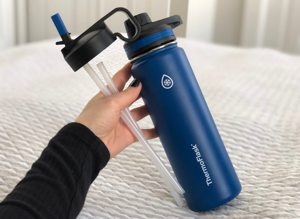 hand holding blue water bottle on top of stripe blanket