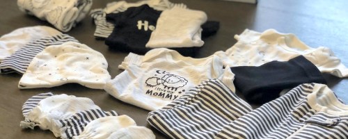 tons of black and white gender neutral baby clothes laying on table