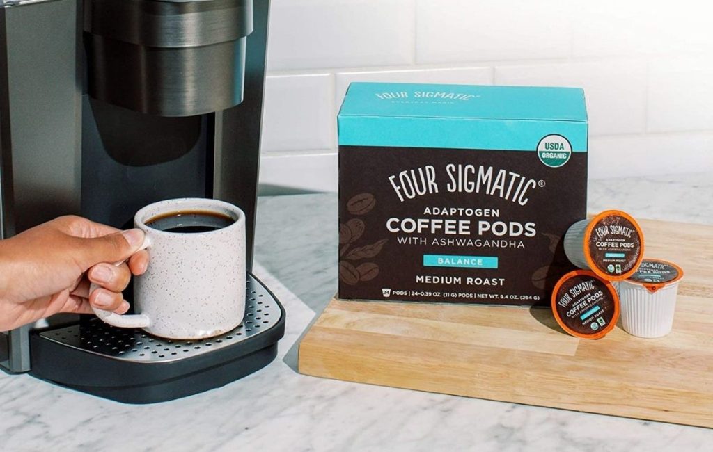 Four Sigmatic Coffee Pods next to brewed cup of coffee on a Keurig maker