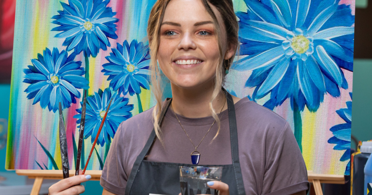 girl wearing a paint smock in front of a floral painting