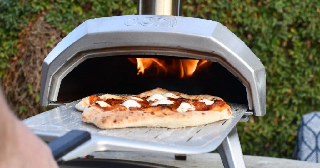 person putting pizza inside Ooni pizza oven 