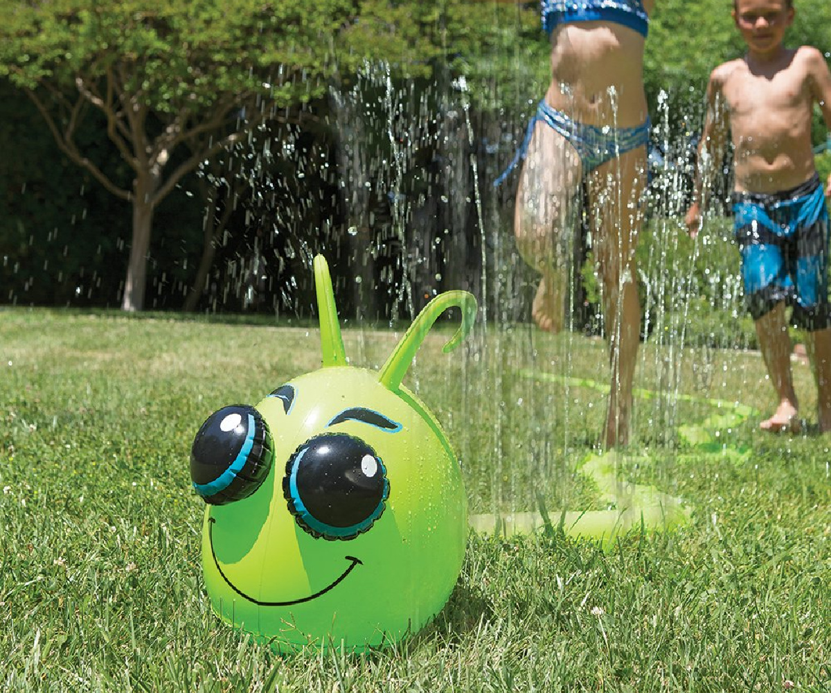 kids running through long caterpillar sprinkler outside on grass