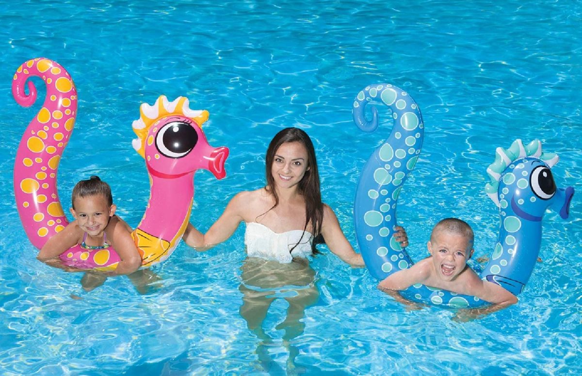 woman in pool with two kids playing on pink and blue seahorse pool noodles