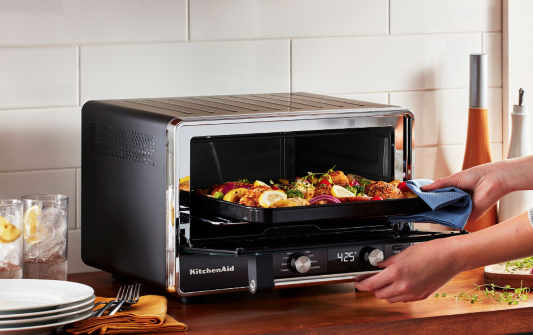 person pulling pizza out of kitchenaid countertop oven