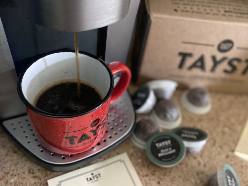 red coffe mug under a keurig next to tayst coffee k-cups